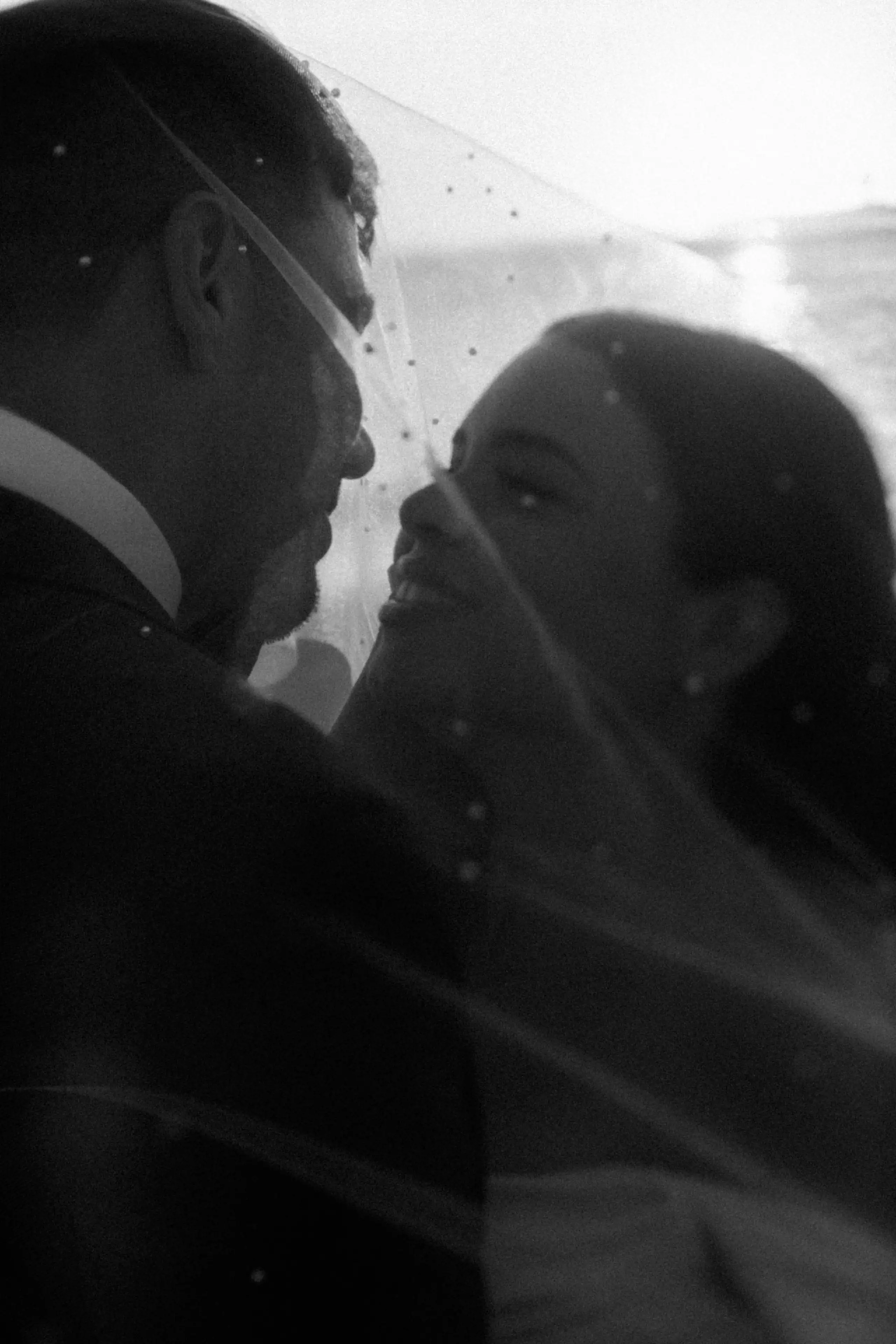A romantic moment between newlyweds in front of a stone and brick mansion with manicured shrubs and a brick pathway.