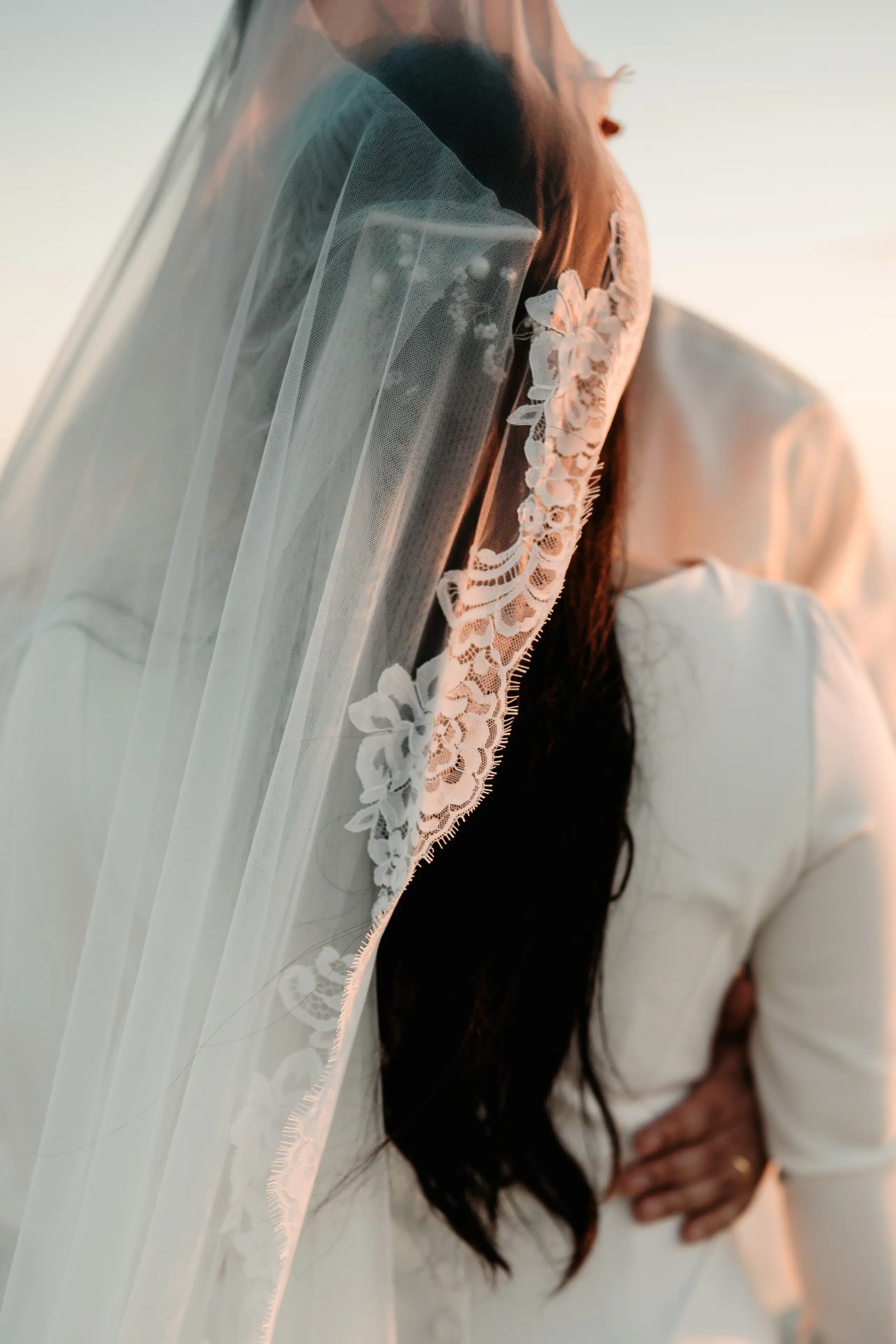 Adult and child walking hand in hand on a beach with pier in background.